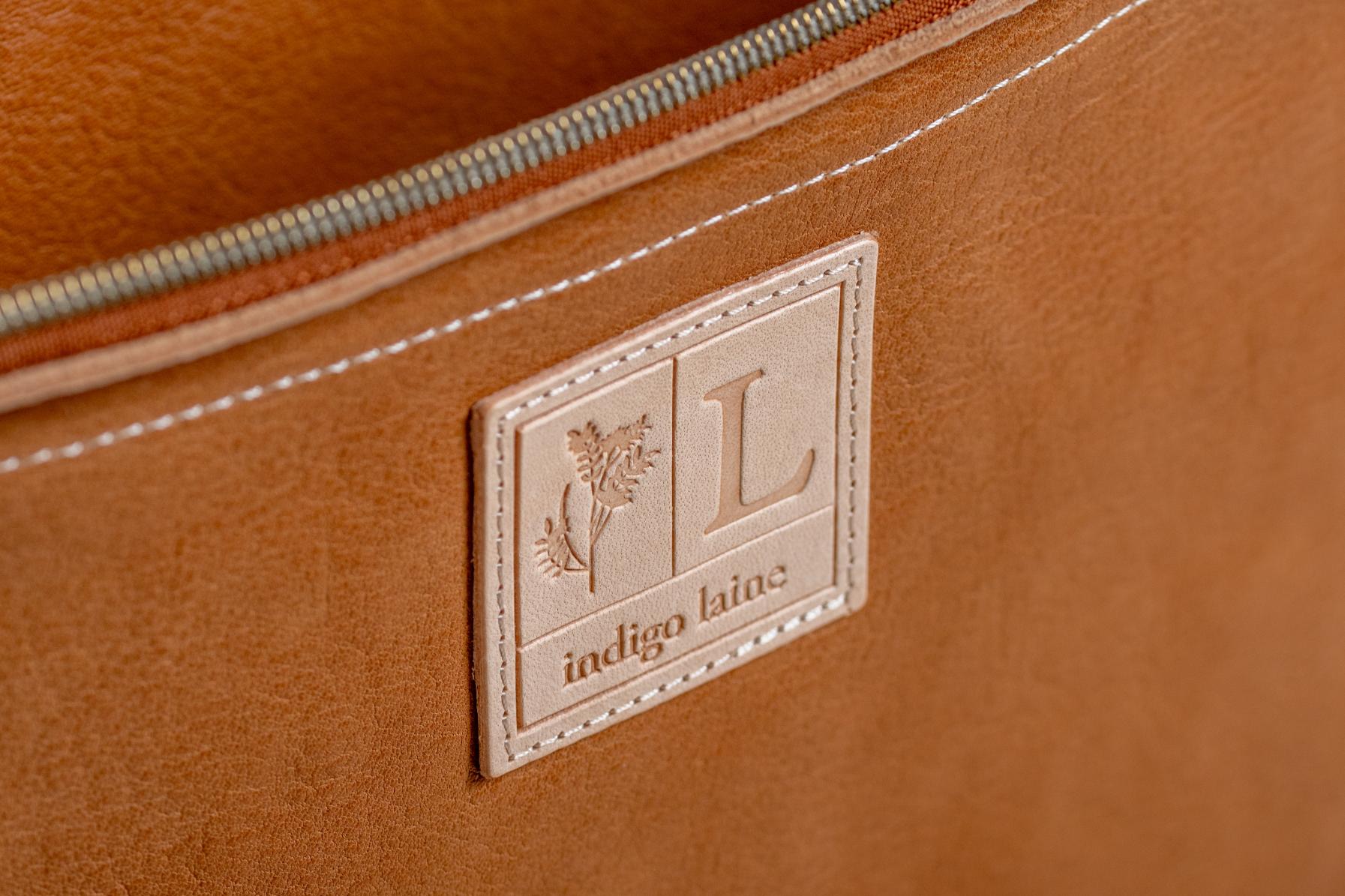 Close-up of Indigo Laine The Laptop Sleeve in Camel, showing the Indigo Laine log and zipper