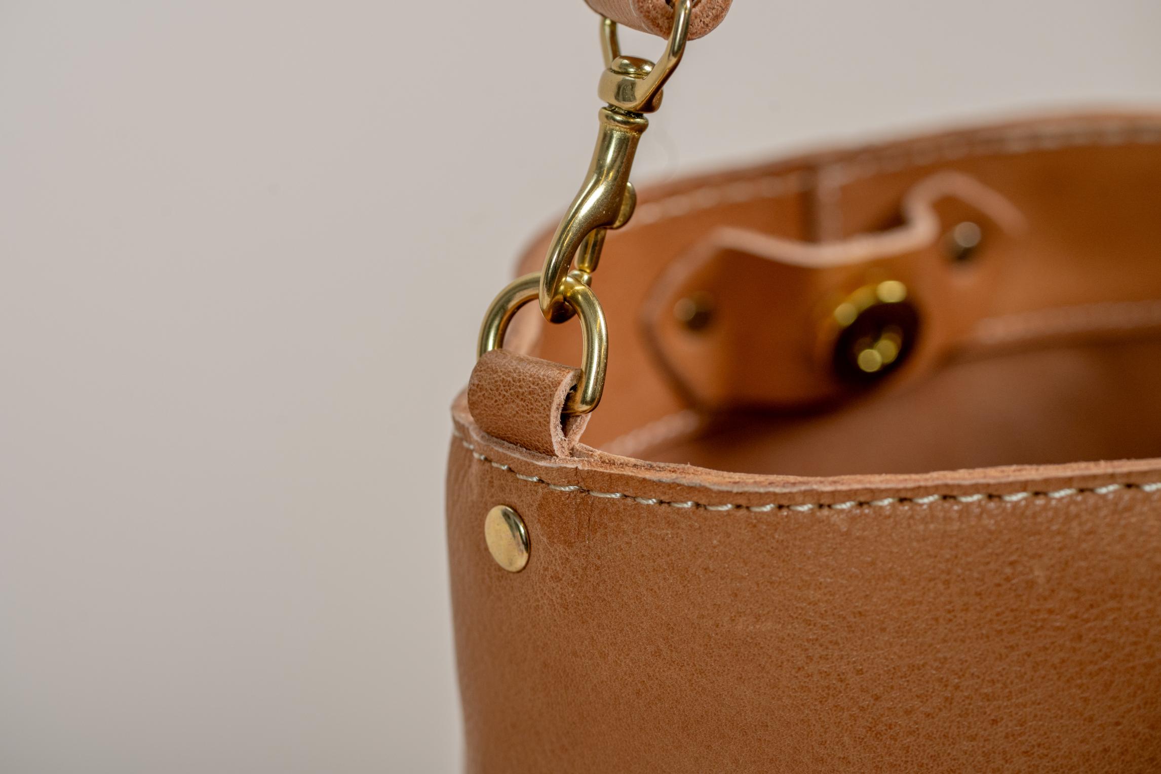 Close-up of leather bag's gold clasp and strap attachment.