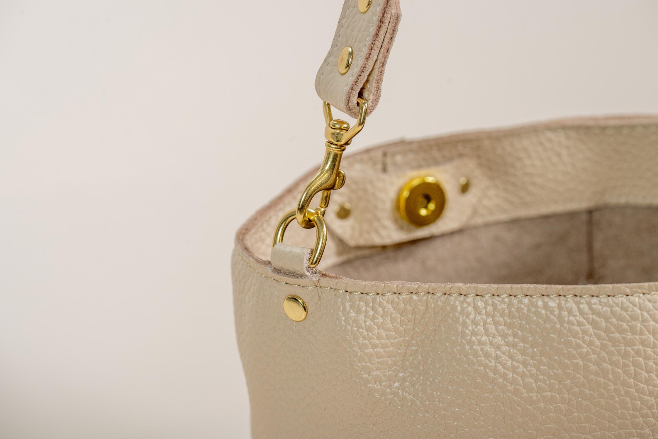 Close-up of cream leather bag's gold clasp and strap attachment