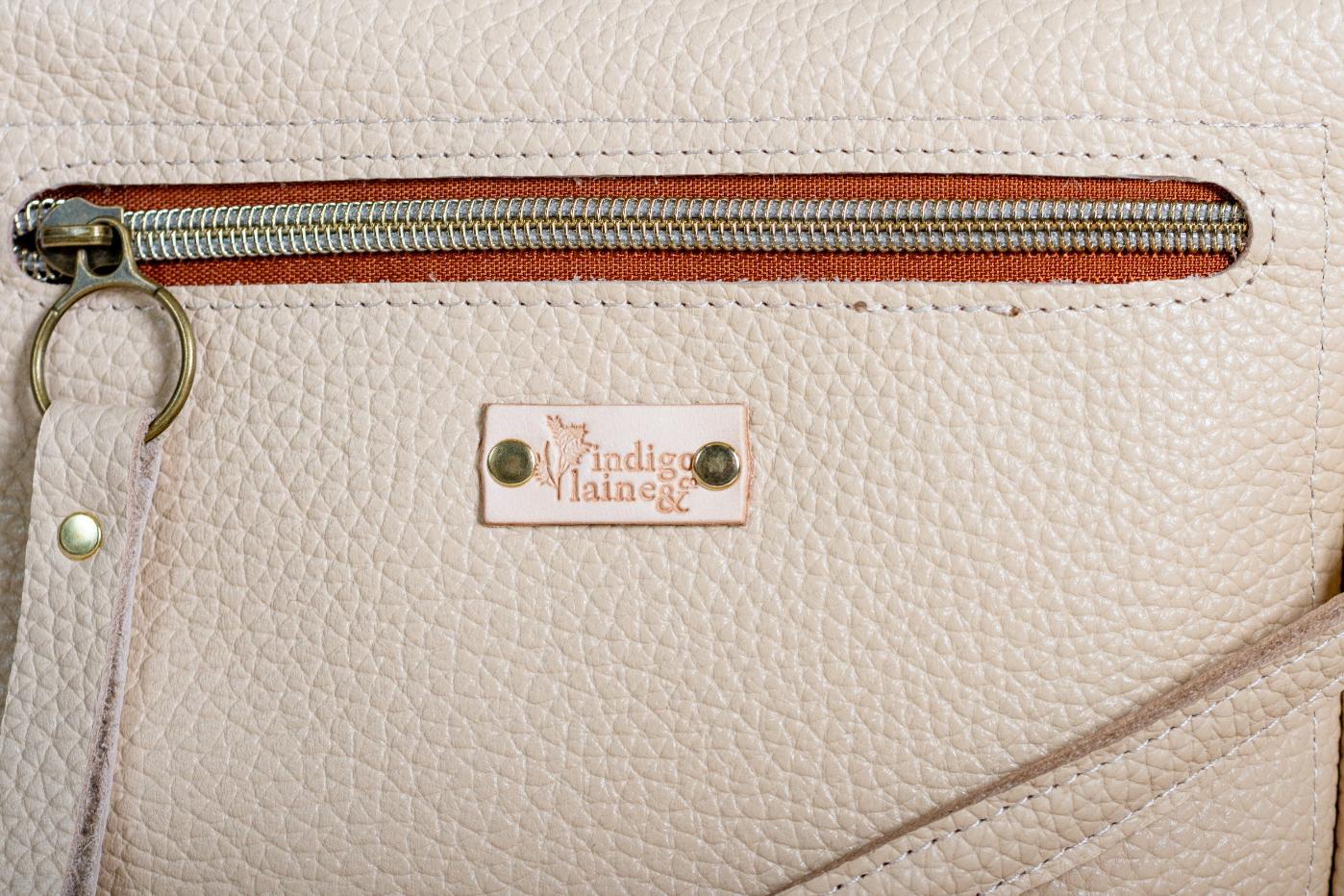 Close-up of The Shelly Crossbody's zip pocket and brand tag in cream